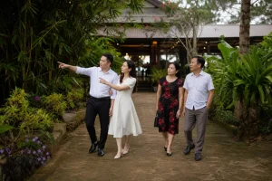 Cặp đôi Việt Nam cùng người thân quan sát khu vực sân vườn và lối di chuyển quanh nhà hàng tiệc cưới tại Gia Nghĩa trong buổi khảo sát địa điểm, thể hiện quá trình đánh giá không g