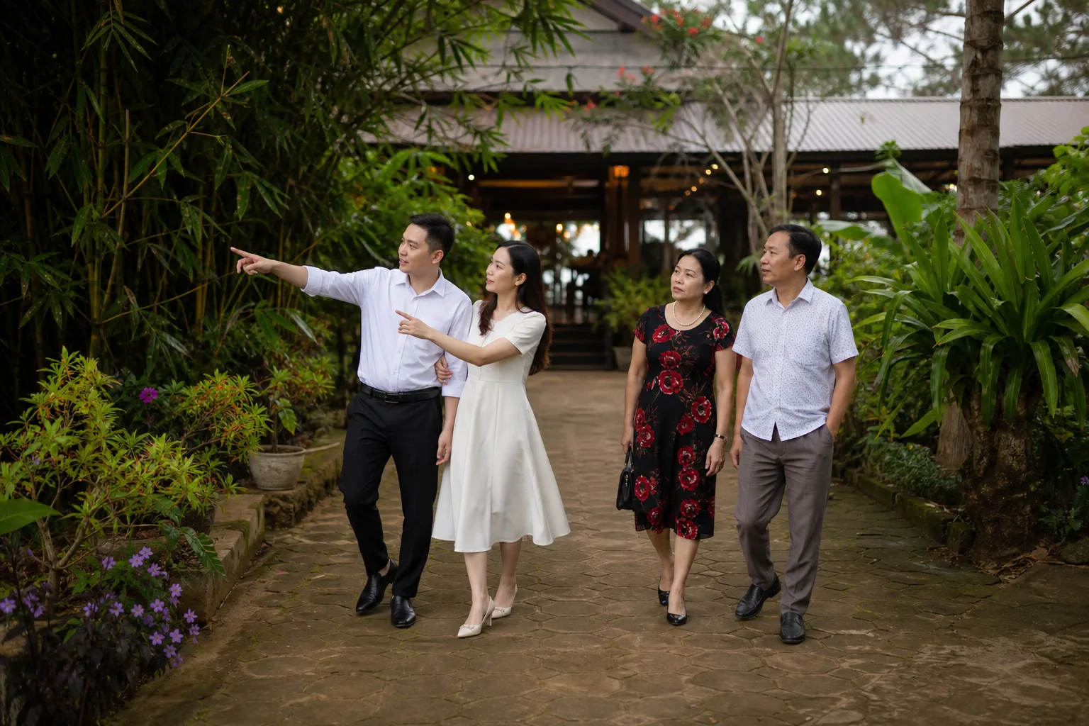 Cặp đôi Việt Nam cùng người thân quan sát khu vực sân vườn và lối di chuyển quanh nhà hàng tiệc cưới tại Gia Nghĩa trong buổi khảo sát địa điểm, thể hiện quá trình đánh giá không g