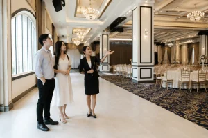 Cô dâu chú rể Việt Nam cùng chuyên viên nhà hàng quan sát toàn bộ sảnh tiệc cưới trống, tập trung trao đổi về cách bố trí không gian, khu vực đón khách và lối di chuyển trước khi l