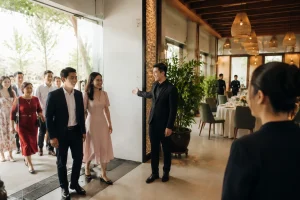 Khách mời Việt Nam bước vào không gian tiệc cưới tại nhà hàng, được nhân viên hướng dẫn nhẹ nhàng ở khu vực lối vào với cảm giác chào đón, thuận tiện và thoải mái trước khi tham dự